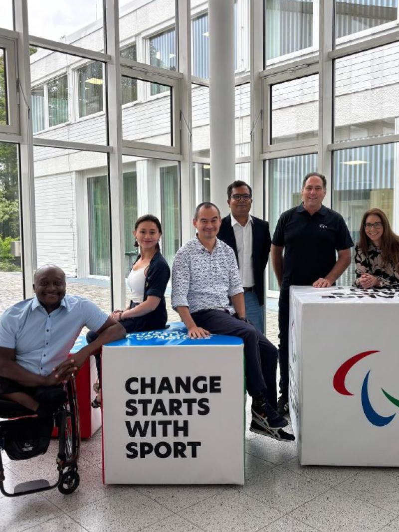 Six people pose for a photograph in front of two blocks that say "Change Starts with Sport" at the IPC Campus in Bonn, Germany
