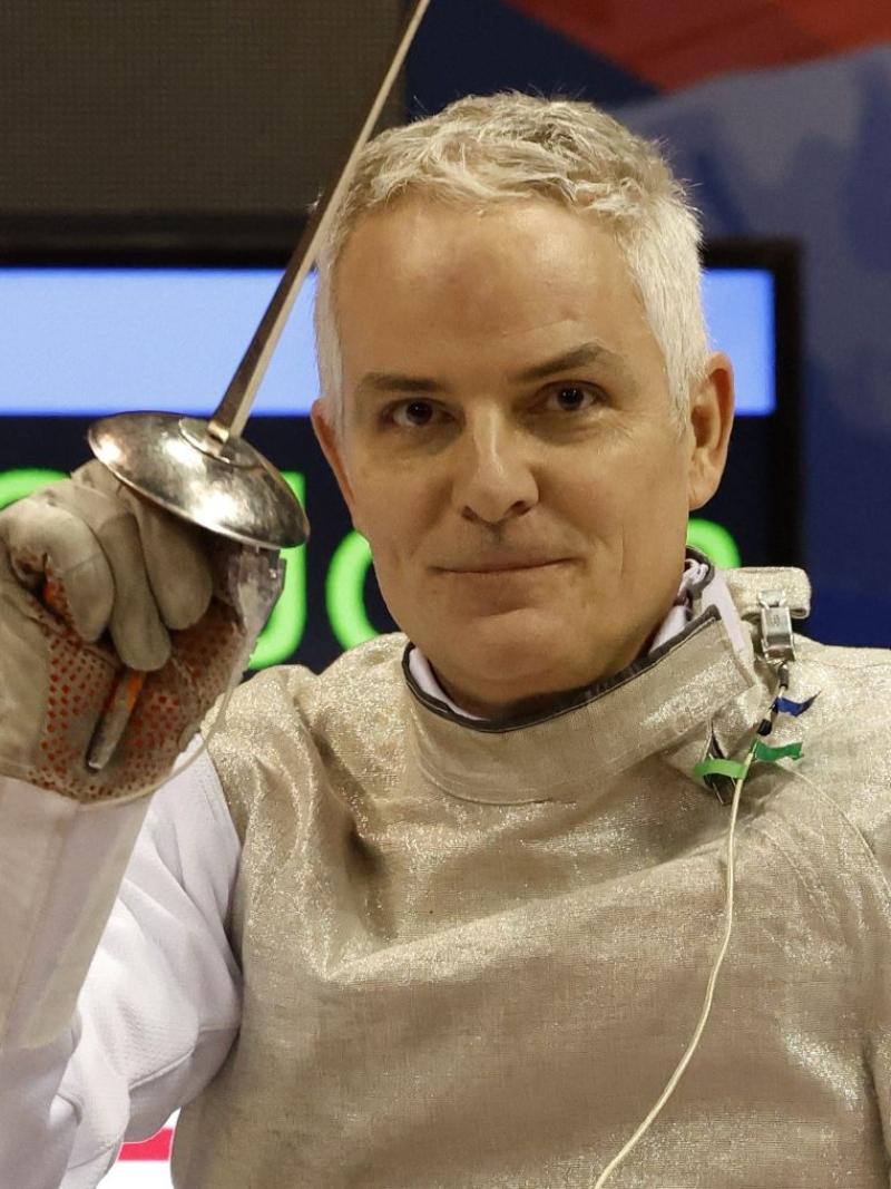 Scott Rodgers smiles for a photo while holding an epee