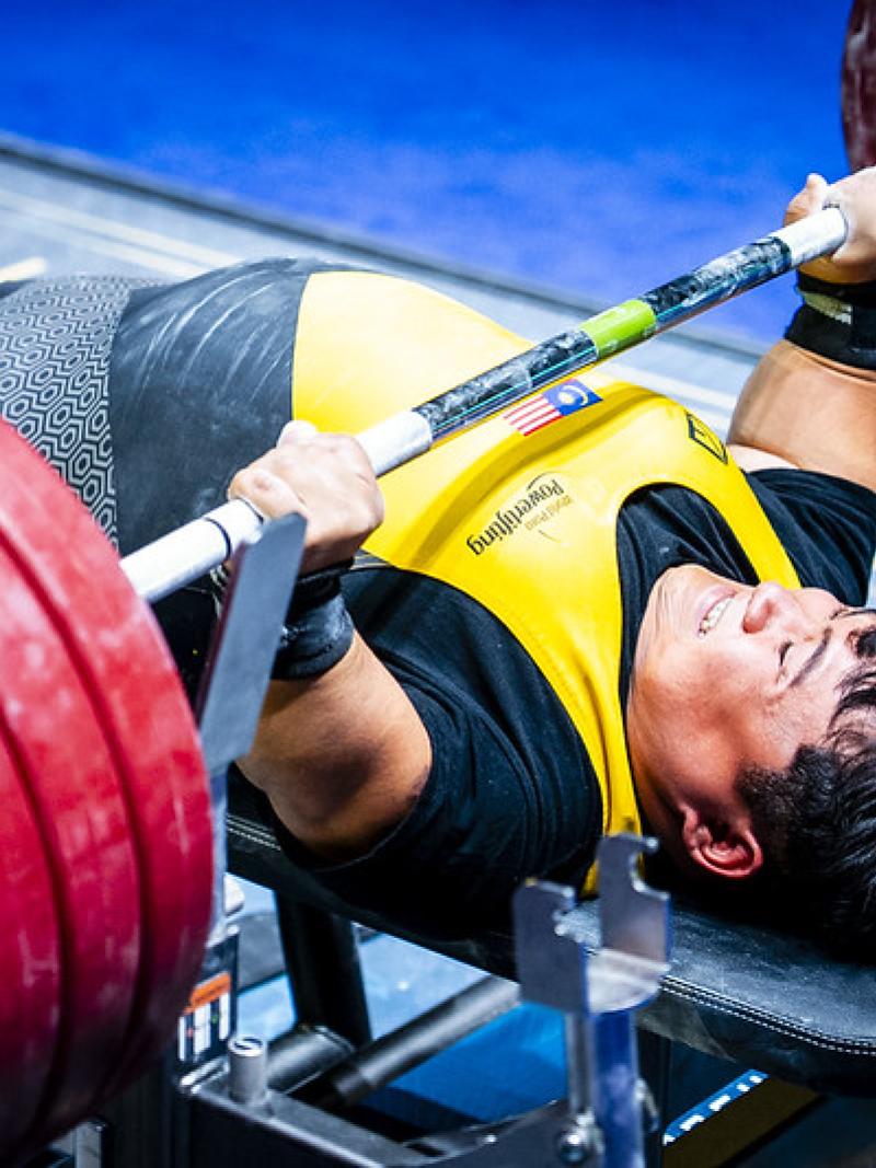 A short stature man lifting weight in a Para powerlifting competition