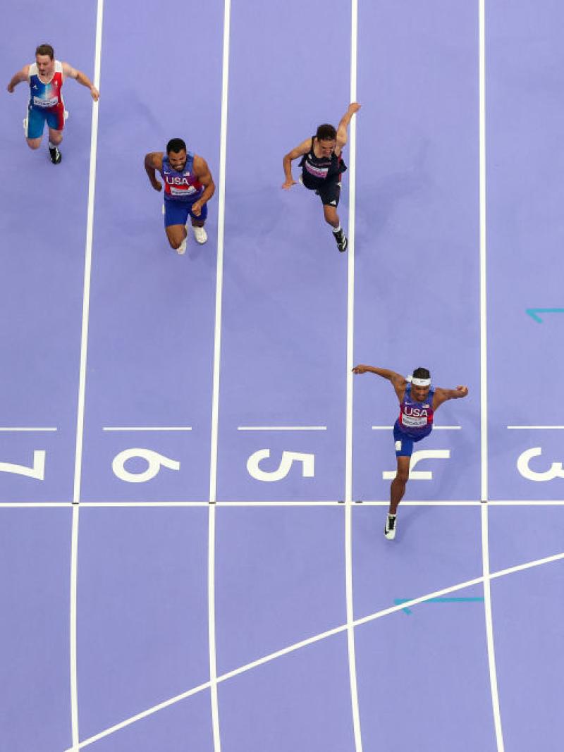 A photo taken from above shows purple athletics track and six athletes racing